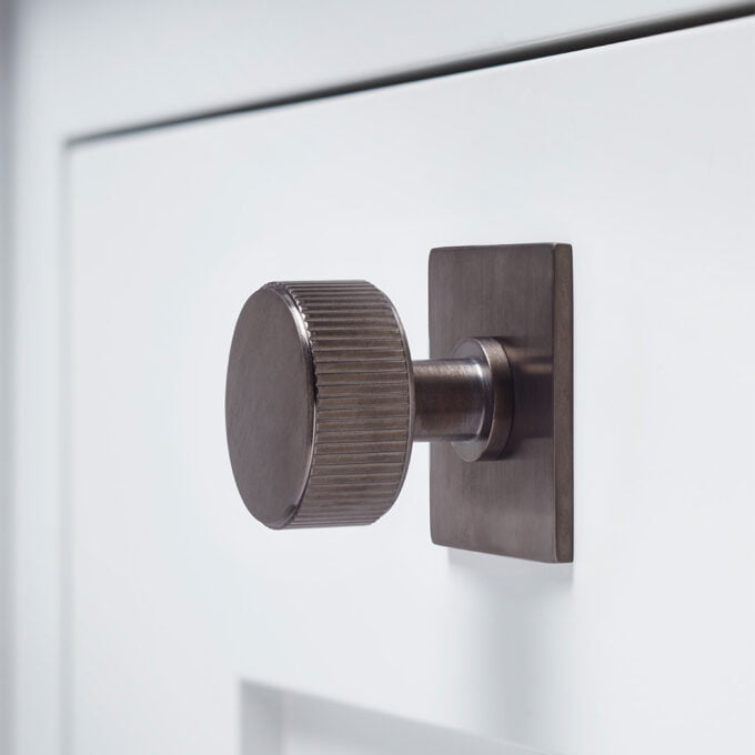 Modern brushed metal cabinet knob on white drawer.