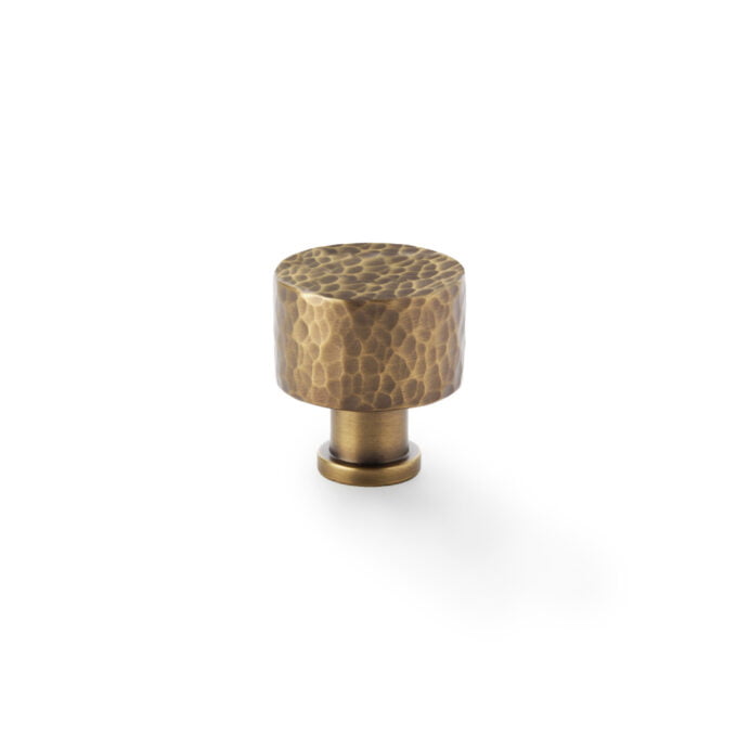 Antique brass cabinet knob with hammered texture on white background.
