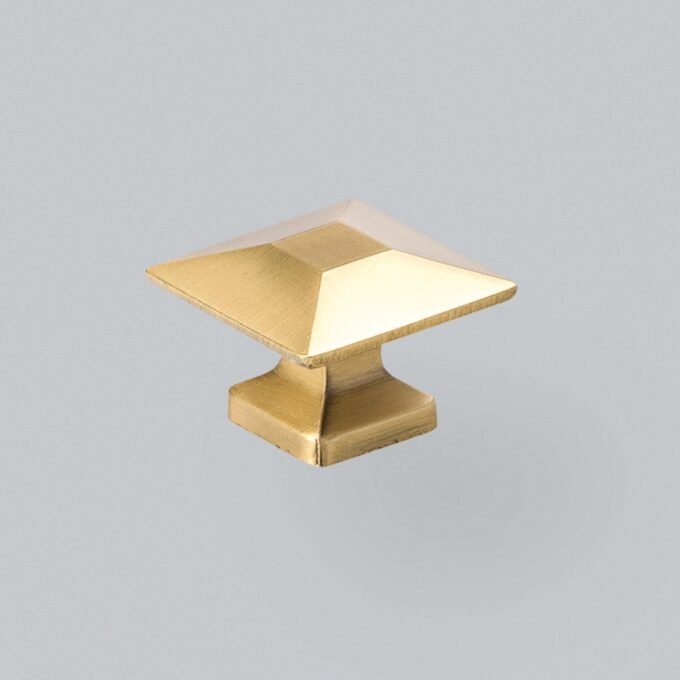 Gold-coloured square cabinet knob on grey background.