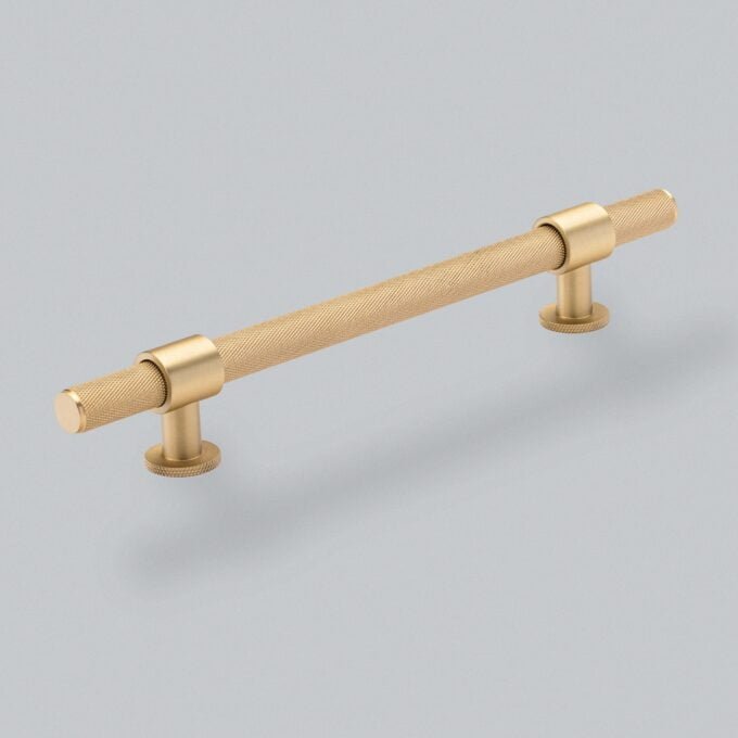 Gold knurled cabinet handle on grey background.