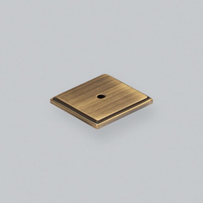 Antique brass square cabinet knob on grey background.