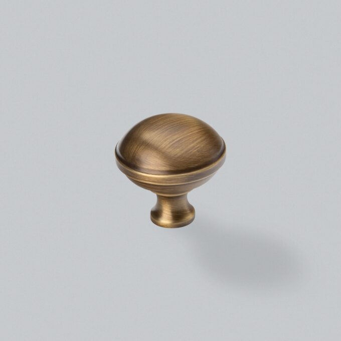 Antique brass cabinet knob on grey background.