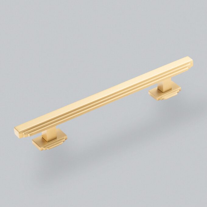 Gold-coloured modern cabinet handle on grey background.