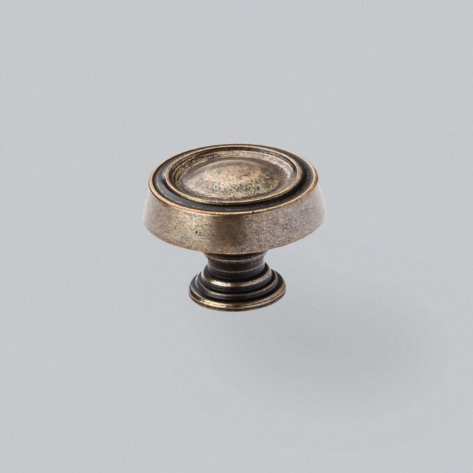 Antique bronze cabinet knob on a grey background.